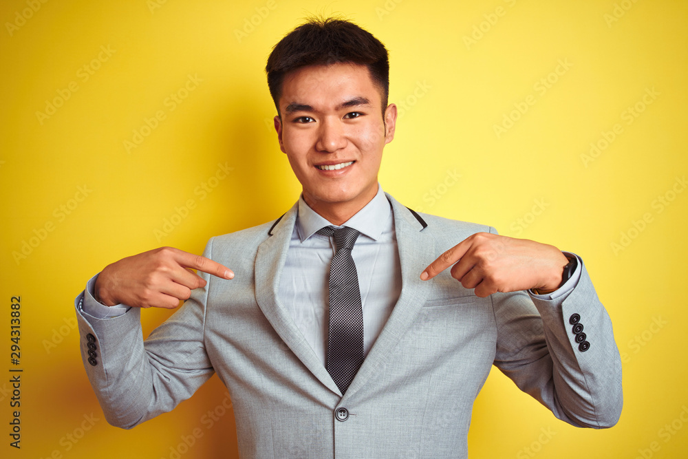 Asian chinese businessman wearing suit and tie standing over isolated yellow background looking confident with smile on face, pointing oneself with fingers proud and happy. Asian chinese businessman wearing suit and tie standing over isolated yellow background looking confident with smile on face, pointing oneself with fingers proud and happy.