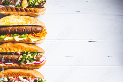 Bilde på lerret Hot dogs with different toppings on white wooden background, top view, copy space