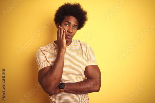 American man with afro hair wearing striped t-shirt standing over isolated yellow background thinking looking tired and bored with depression problems with crossed arms. © Krakenimages.com