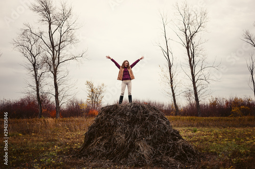 a young woman stands on a haystack in the fall