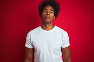 Young american man with afro hair wearing white t-shirt standing over isolated red background with serious expression on face. Simple and natural looking at the camera.