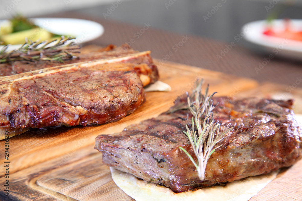 Medium-roasted steak cut into pieces on a wooden board with sauce and seasonings. Delicious steak. Beef steak medium rare on vegetable cushion. Beef steak on wooden plate. 