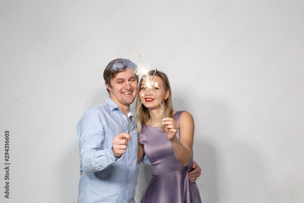 Celebration, party and holiday concept - Happy man and woman hugging over grey background with sparklers Celebration, party and holiday concept - Happy man and woman hugging over grey background with sparklers