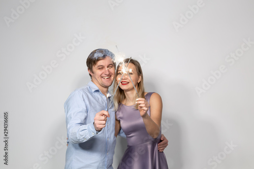 Celebration, party and holiday concept - Happy man and woman hugging over grey background with sparklers