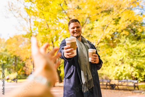 man brings coffee to friend drink to go outdoors autumn city park