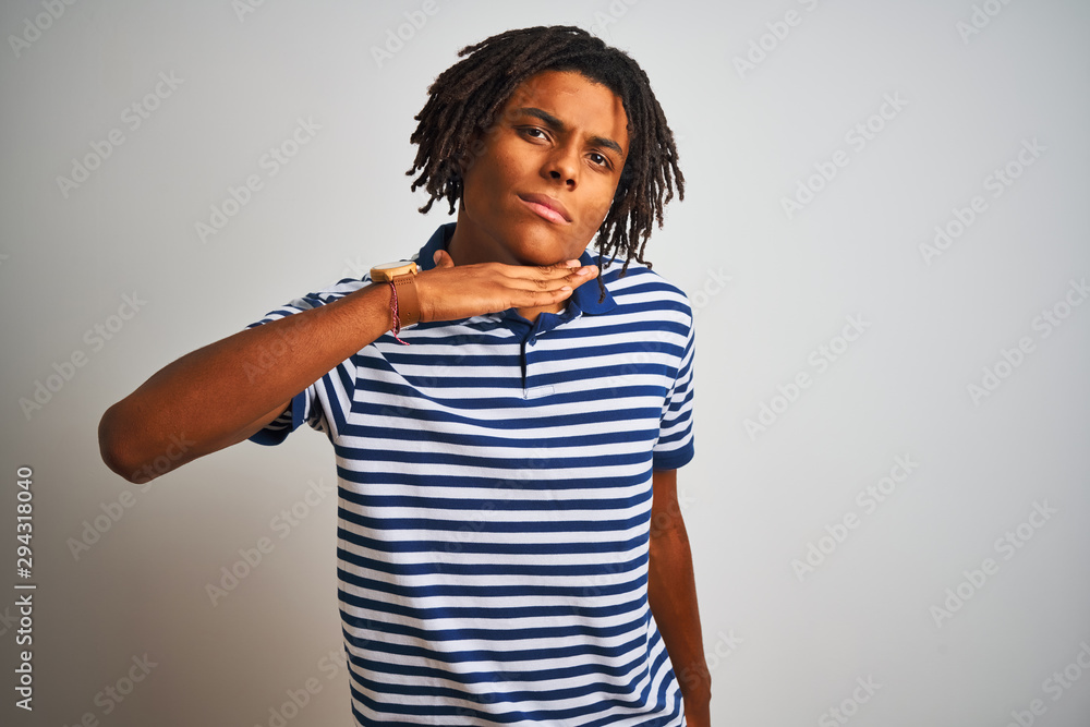 Afro man with dreadlocks wearing striped blue polo standing over isolated white background cutting throat with hand as knife, threaten aggression with furious violence Afro man with dreadlocks wearing striped blue polo standing over isolated white background cutting throat with hand as knife, threaten aggression with furious violence