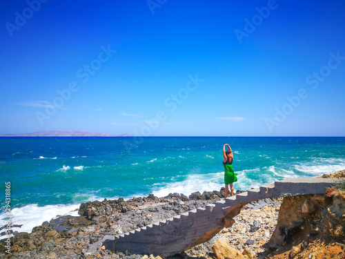 Girl takes the energy of the sea. Girl on a background of waves pulls her hands up the wind inflates her dress. Stressed woman relaxing. Health  energy and success concept.