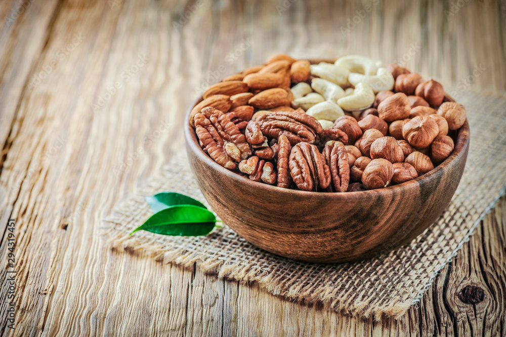 Nuts mix in a wooden bowl. Nuts concept. Walnut heart with green leaves Nuts mix in a wooden bowl. Nuts concept. Walnut heart with green leaves