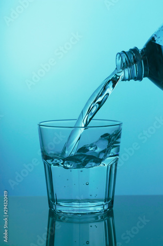 Water is poured into a glass on a blue background, close-up