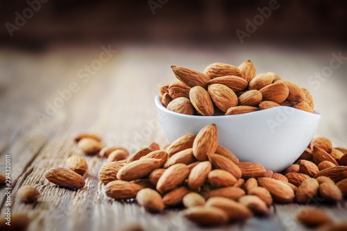 Almonds in white porcelain bowl on wooden table. Almond concept with copyspace. © Milan