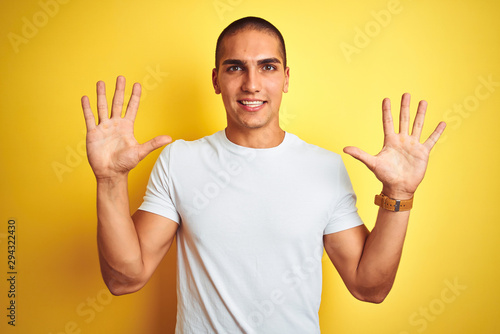 Young caucasian man wearing casual white t-shirt over yellow isolated background showing and pointing up with fingers number ten while smiling confident and happy.