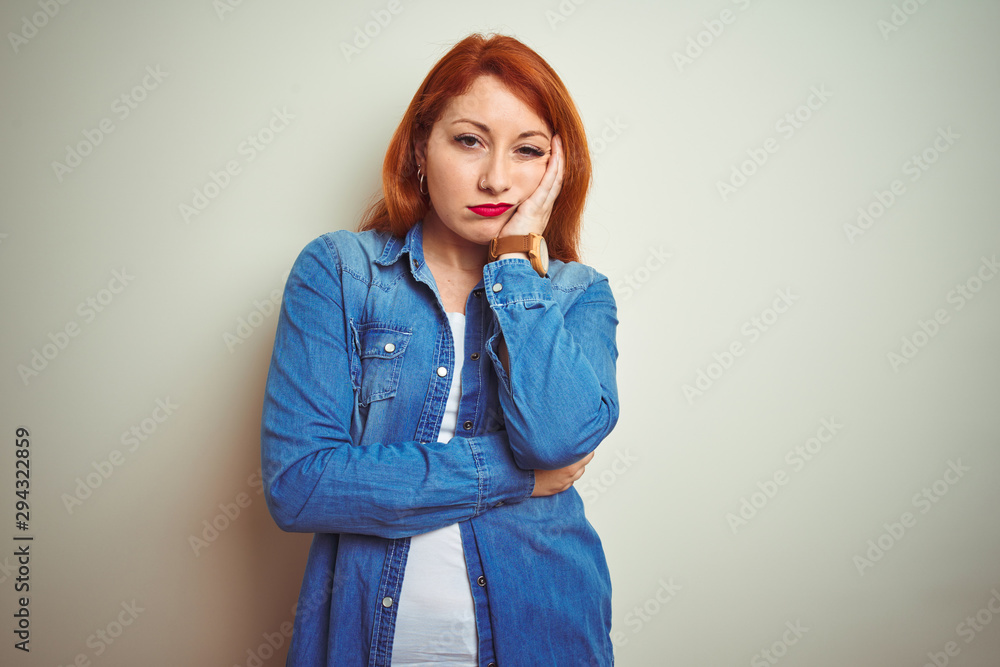 Young beautiful redhead woman wearing denim shirt standing over white isolated background thinking looking tired and bored with depression problems with crossed arms. Young beautiful redhead woman wearing denim shirt standing over white isolated background thinking looking tired and bored with depression problems with crossed arms.
