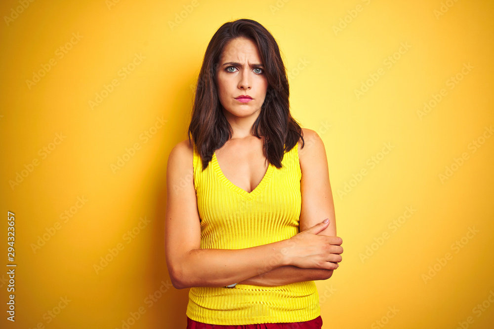 Young beautiful woman wearing t-shirt standing over yellow isolated background skeptic and nervous, disapproving expression on face with crossed arms. Negative person. Young beautiful woman wearing t-shirt standing over yellow isolated background skeptic and nervous, disapproving expression on face with crossed arms. Negative person.