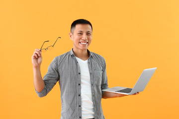 Male Asian programmer with laptop on color background