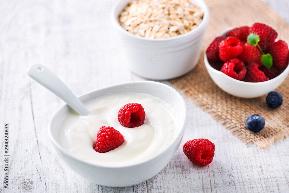 Fresh white yoghurt with raw forest fruits. Rasberries in white yoghurt in bowl on white table. Best meal for healthy breakfast. Fresh white yoghurt with raw forest fruits. Rasberries in white yoghurt in bowl on white table. Best meal for healthy breakfast.