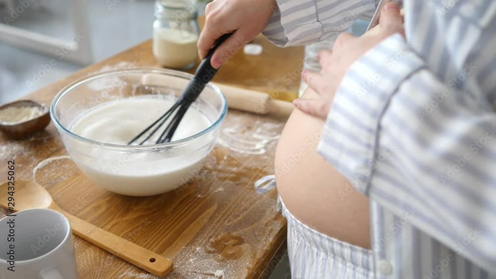 Closeup Of Pregnant Woman Whisking Milk In Bowl While Baking On Kitchen Closeup Of Pregnant Woman Whisking Milk In Bowl While Baking On Kitchen