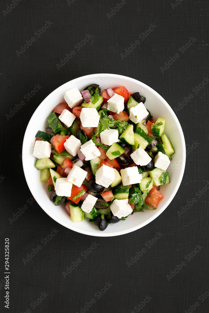 Homemade Shepherd's salad with cucumbers, feta and parsley in a white bowl over black surface, top view. From above, overhead, flat lay. Homemade Shepherd's salad with cucumbers, feta and parsley in a white bowl over black surface, top view. From above, overhead, flat lay.