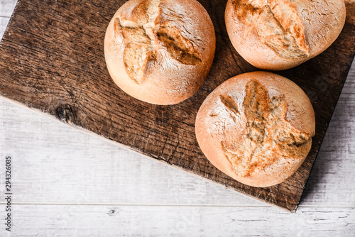 Fresh buns and on wood board. Fresh Light rustic loaf of tasty and  bread on rold white table. photo