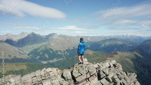A young brave man standing on rocky cliff edge and looking away at beautiful natural landscape with mountain ranges and overgreen valleys. Aerial drone view of Caucasian national Park. sport lifestyle photo