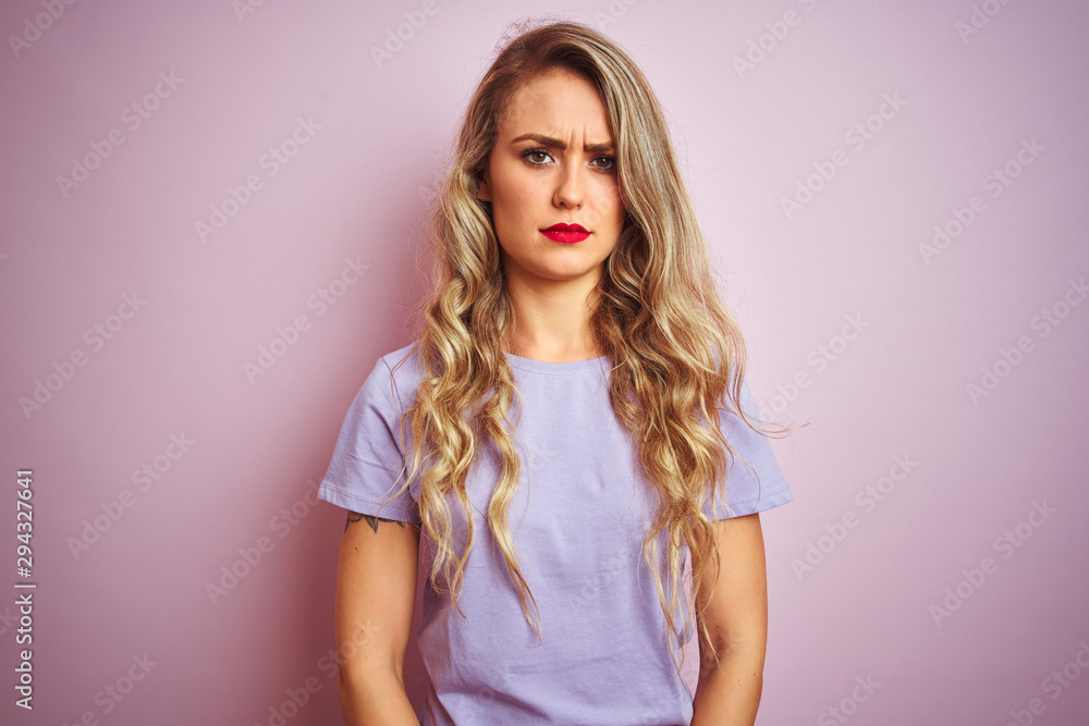Young beautiful woman wearing purple t-shirt standing over pink isolated background skeptic and nervous, frowning upset because of problem. Negative person.