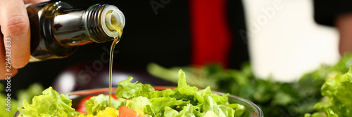 Cook holds bottle in hand and trickles olive extra virgin oil into fresh vegetable salad with vitamins. Raw food and vegetarian in modern society vegan is popular concept. photo