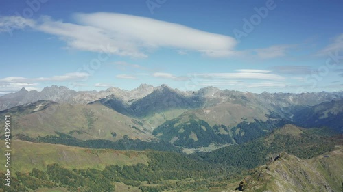 A young brave man standing on rocky cliff edge and looking away at beautiful natural landscape with mountain ranges and overgreen valleys. Aerial drone view of Caucasian national Park. sport lifestyle photo