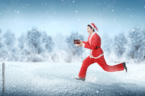 Asian man in Santa costume running while holding the gift box