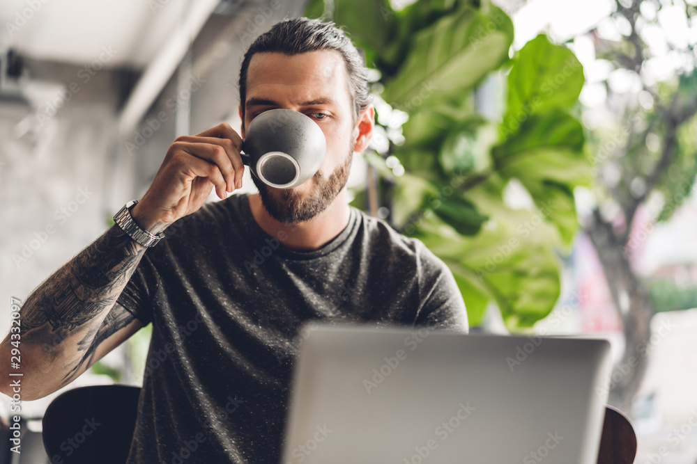 Fototapeta premium Handsome bearded hipster man use and looking at laptop computer with coffee at table in cafe.Communication and technology concept
