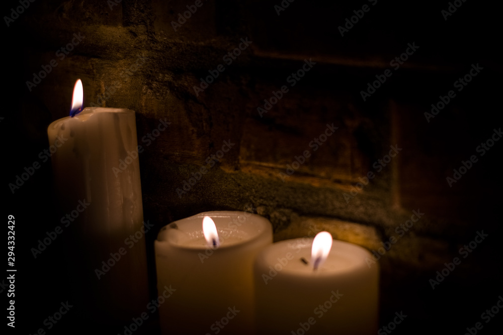 Background or texture of large white burning candles in dark room near brick wall. Holiday. Helloween. Background or texture of large white burning candles in dark room near brick wall. Holiday. Helloween.