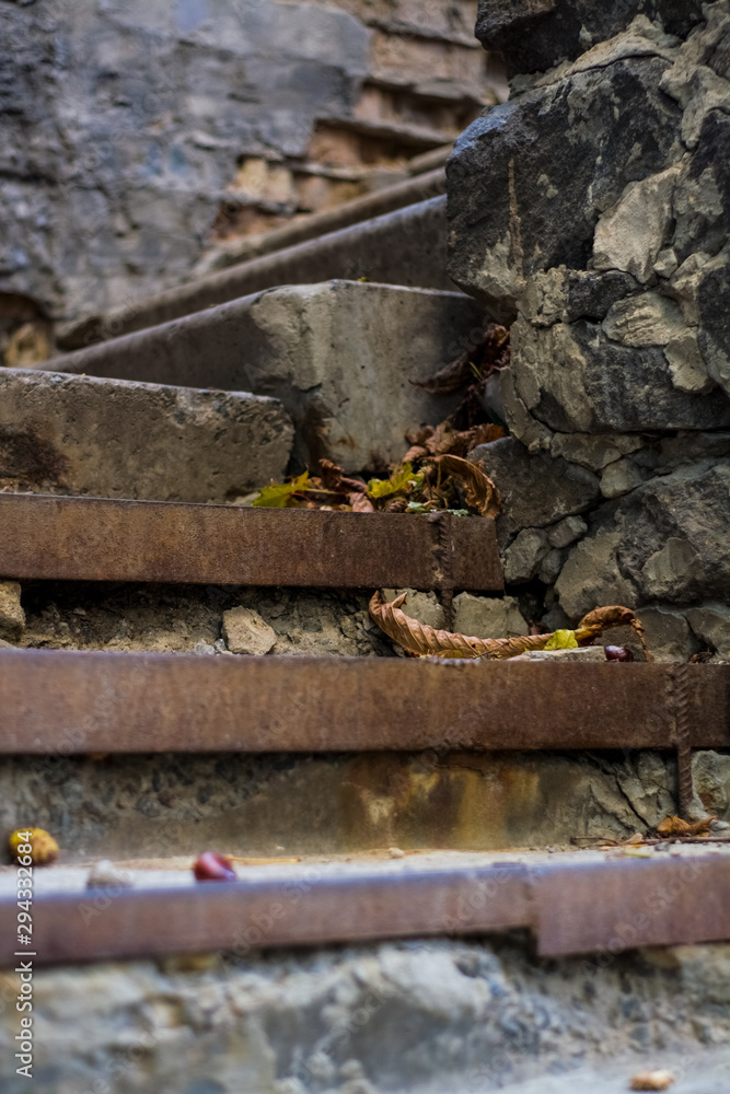 Background or texture of broken old, concrete steps on street with metal crossbars and fallen autumn, yellow leaves. Stone wall. Background or texture of broken old, concrete steps on street with metal crossbars and fallen autumn, yellow leaves. Stone wall.