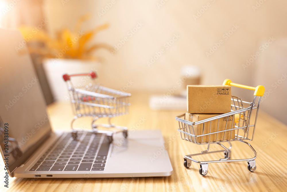 Online shopping and delivery service concept.Brown paper boxs in a shopping cart with laptop keyboard on wood table in office background.Easy shopping with finger tips for consumers.