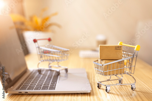 Online shopping and delivery service concept.Brown paper boxs in a shopping cart with laptop keyboard on wood table in office background.Easy shopping with finger tips for consumers. photo