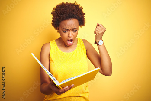 African american woman reading a book over yellow isolated background annoyed and frustrated shouting with anger, crazy and yelling with raised hand, anger concept