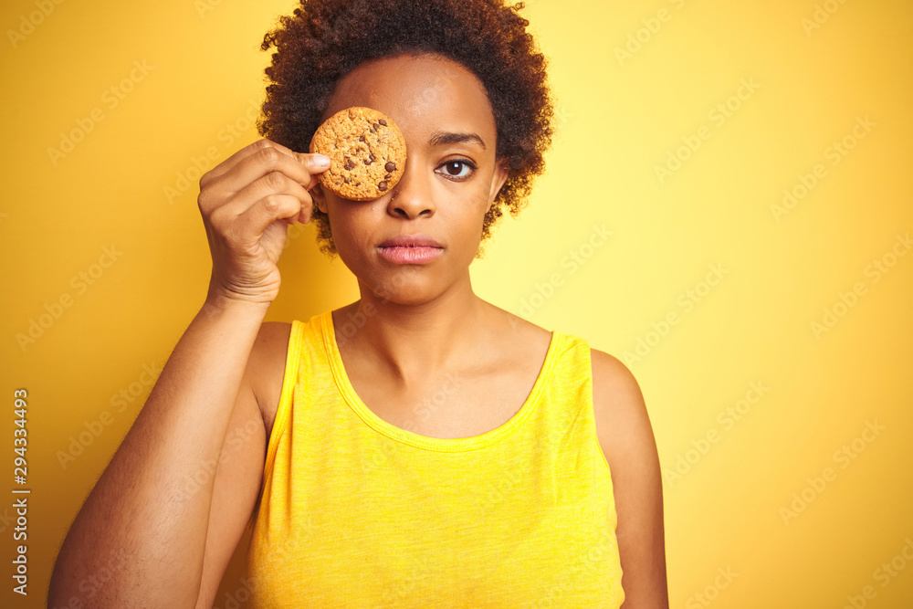 Naklejka premium African american woman holding chocolate chips cookie over yellow background with a confident expression on smart face thinking serious