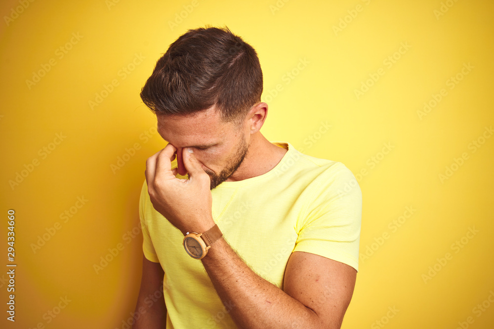 Young handsome man wearing casual yellow t-shirt over yellow isolated background tired rubbing nose and eyes feeling fatigue and headache. Stress and frustration concept. Young handsome man wearing casual yellow t-shirt over yellow isolated background tired rubbing nose and eyes feeling fatigue and headache. Stress and frustration concept.