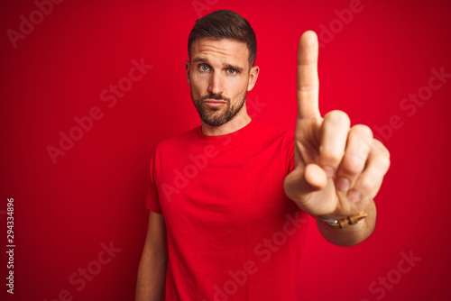 Young handsome man wearing casual t-shirt over red isolated background Pointing with finger up and angry expression, showing no gesture © Krakenimages.com