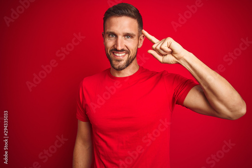 Young handsome man wearing casual t-shirt over red isolated background Smiling pointing to head with one finger, great idea or thought, good memory