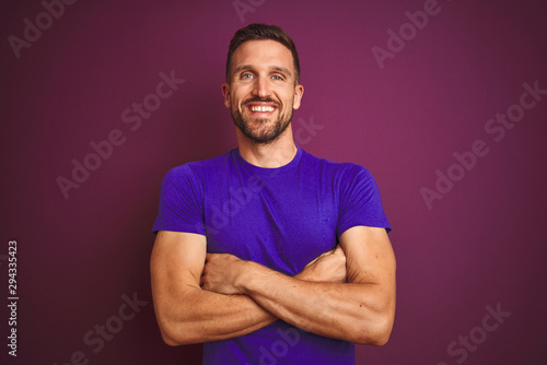 Young man wearing casual purple t-shirt over lilac isolated background happy face smiling with crossed arms looking at the camera. Positive person.