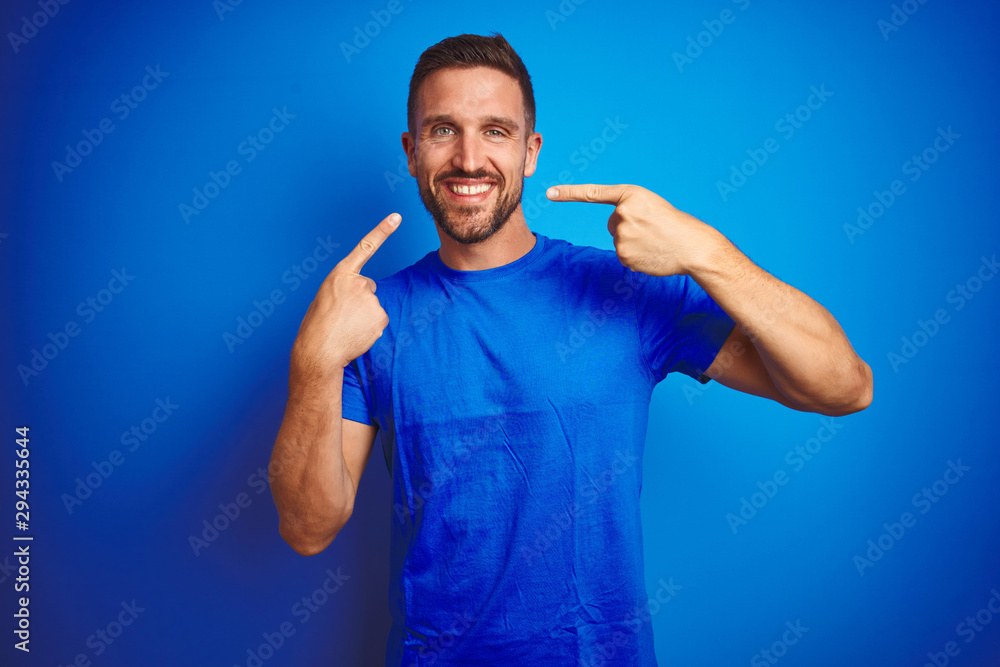 Young handsome man wearing casual t-shirt over blue isolated background smiling cheerful showing and pointing with fingers teeth and mouth. Dental health concept. Young handsome man wearing casual t-shirt over blue isolated background smiling cheerful showing and pointing with fingers teeth and mouth. Dental health concept.