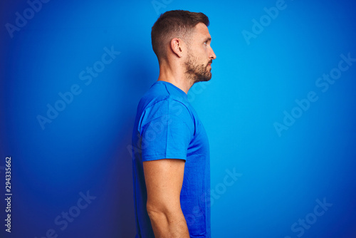 Young handsome man wearing casual t-shirt over blue isolated background looking to side, relax profile pose with natural face with confident smile.