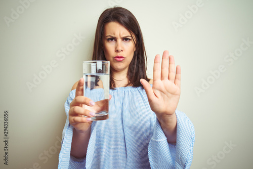 Young beautiful woman drinking a glass of fresh water over isolated background with open hand doing stop sign with serious and confident expression  defense gesture