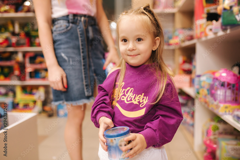 Adorable little girl with mom shopping for toys. Cute female in toy store. Happy young girl selecting toy
