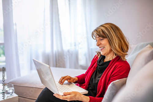 Senior white woman sitting on couch using laptop computer. Technology gets easier by the day. Pretty senior woman at home using laptop. Happy senior woman using laptop while relaxing at home