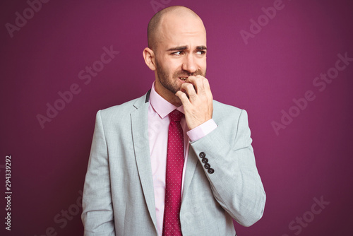 Young business man wearing suit and tie over purple isolated background looking stressed and nervous with hands on mouth biting nails. Anxiety problem. © Krakenimages.com