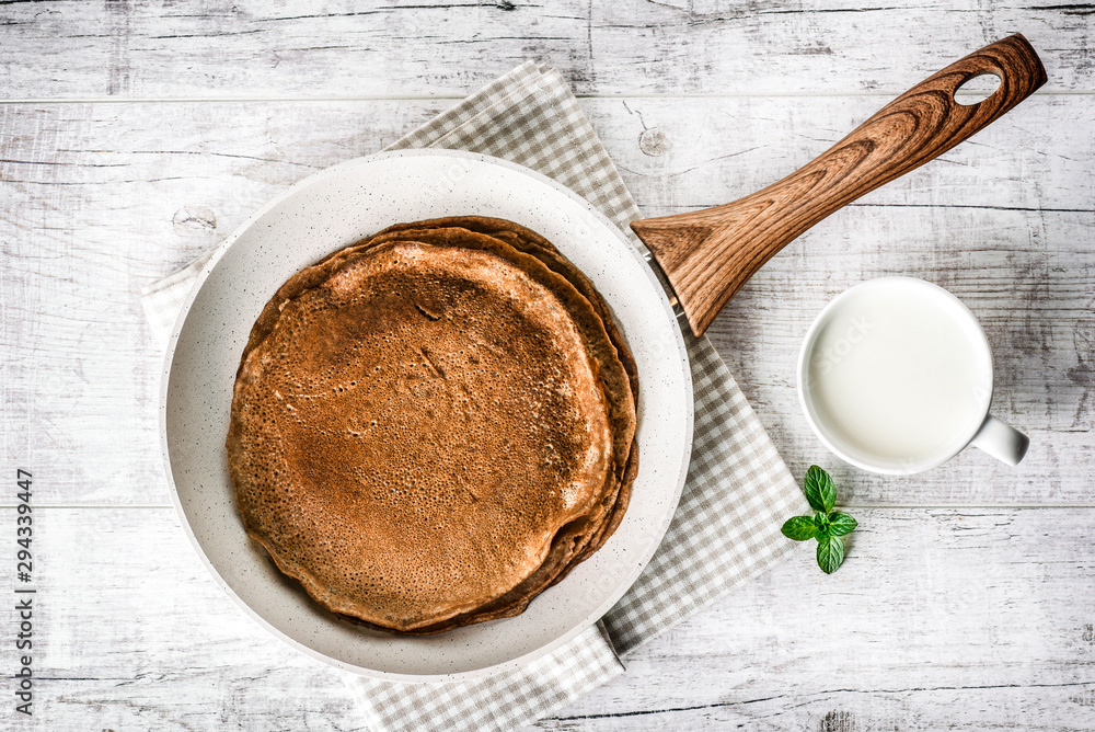 Frying pan with pancake and jar of milak with green mint leaf on white old table. Pancakes in frying pan. Frying pan with pancake and jar of milak with green mint leaf on white old table. Pancakes in frying pan.