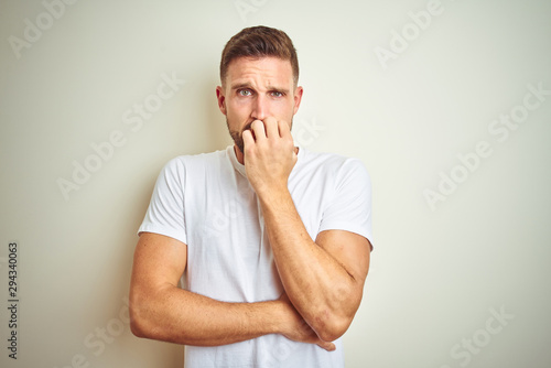 Young handsome man wearing casual white t-shirt over isolated background looking stressed and nervous with hands on mouth biting nails. Anxiety problem.