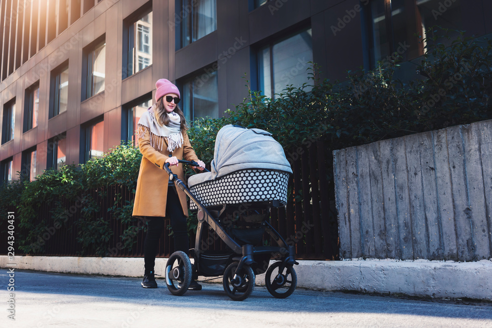 Obraz premium Construction of living blocks for young parents with children. Attractive city environment in calm district for families with kids. Woman enjoying maternity and walking with baby stroller down street.
