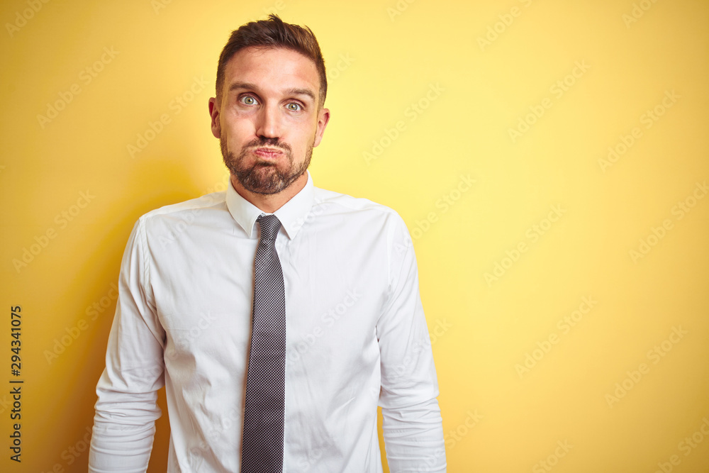 Young handsome business man wearing elegant white shirt over yellow isolated background puffing cheeks with funny face. Mouth inflated with air, crazy expression. Young handsome business man wearing elegant white shirt over yellow isolated background puffing cheeks with funny face. Mouth inflated with air, crazy expression.
