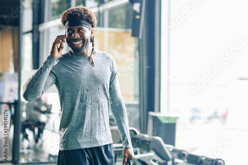 Fototapeta Naklejka Na Ścianę i Meble -  Portrait of handsome young Black man talking on phone after intense training in gym