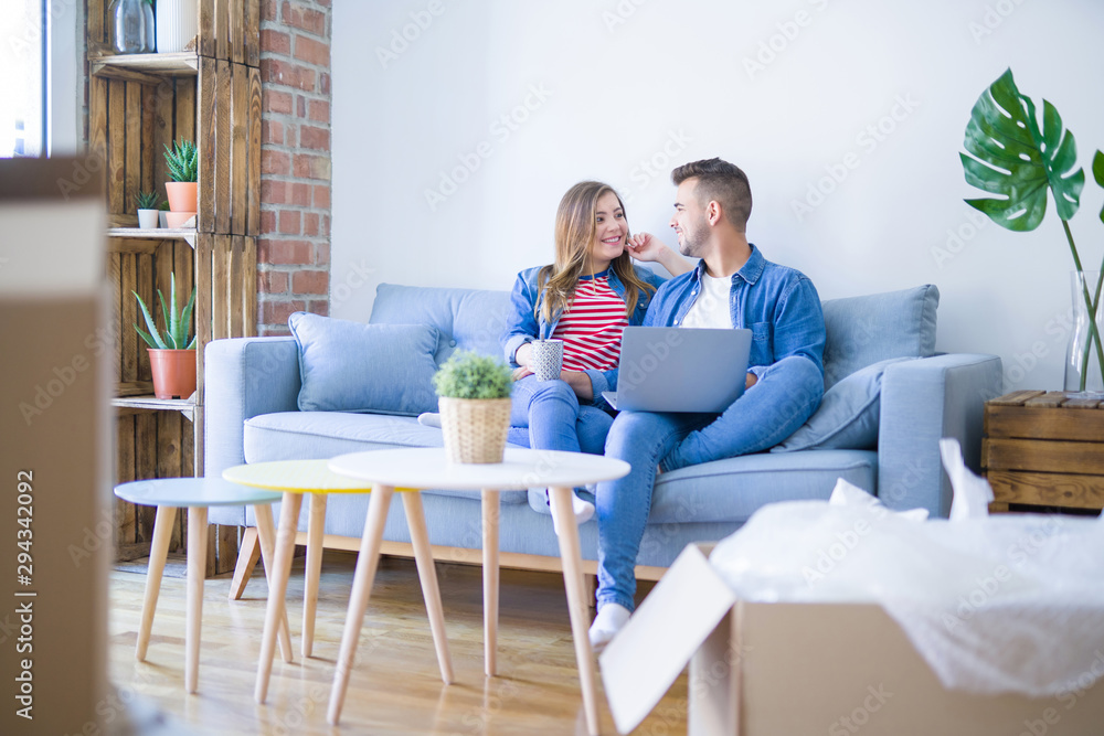 Young couple relaxing sitting on the sofa using the computer laptop around cardboard boxes, very happy moving to a new house Young couple relaxing sitting on the sofa using the computer laptop around cardboard boxes, very happy moving to a new house